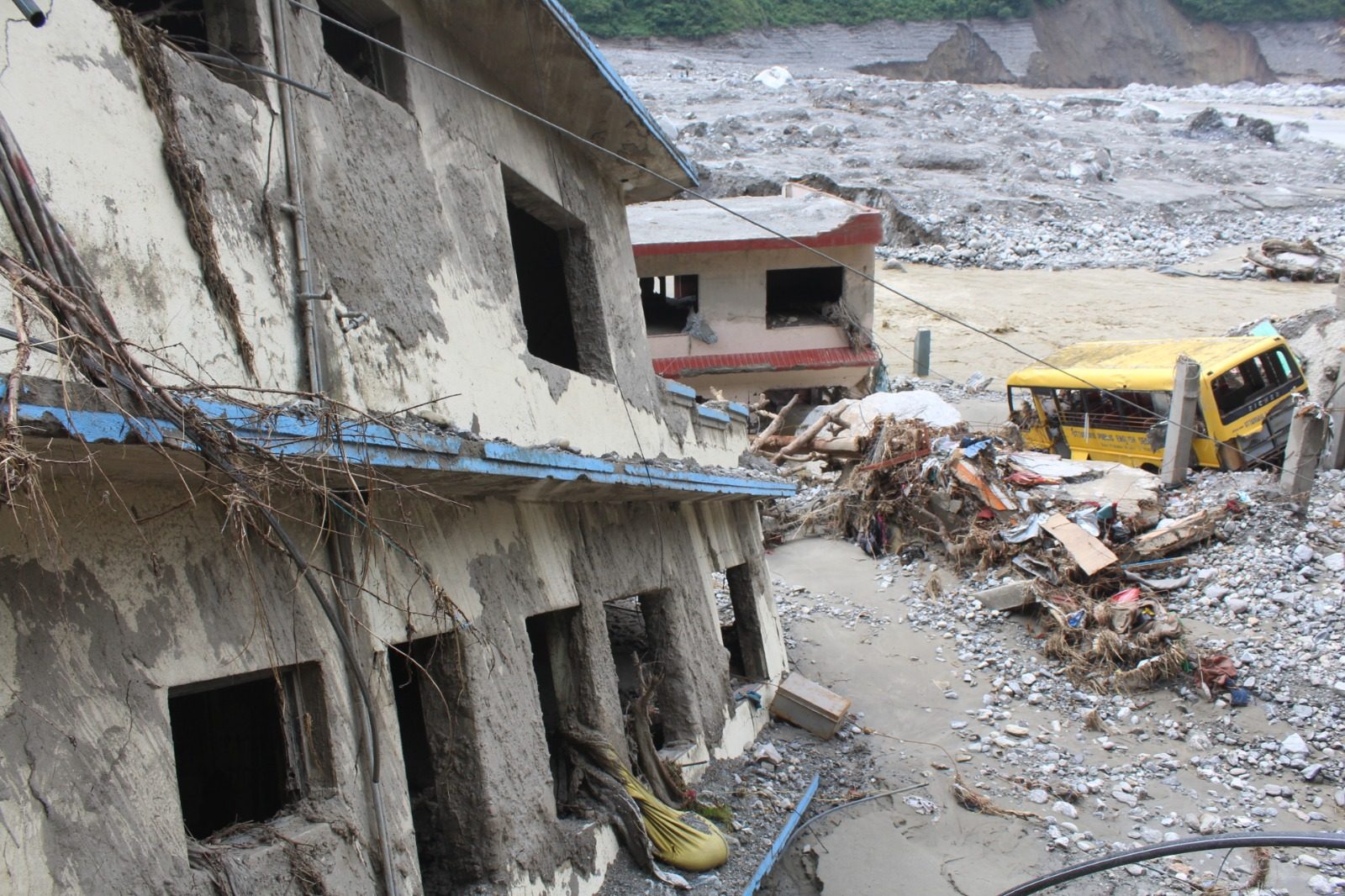 A yellow school bus half buried in debris beside the shells of damaged buildings.