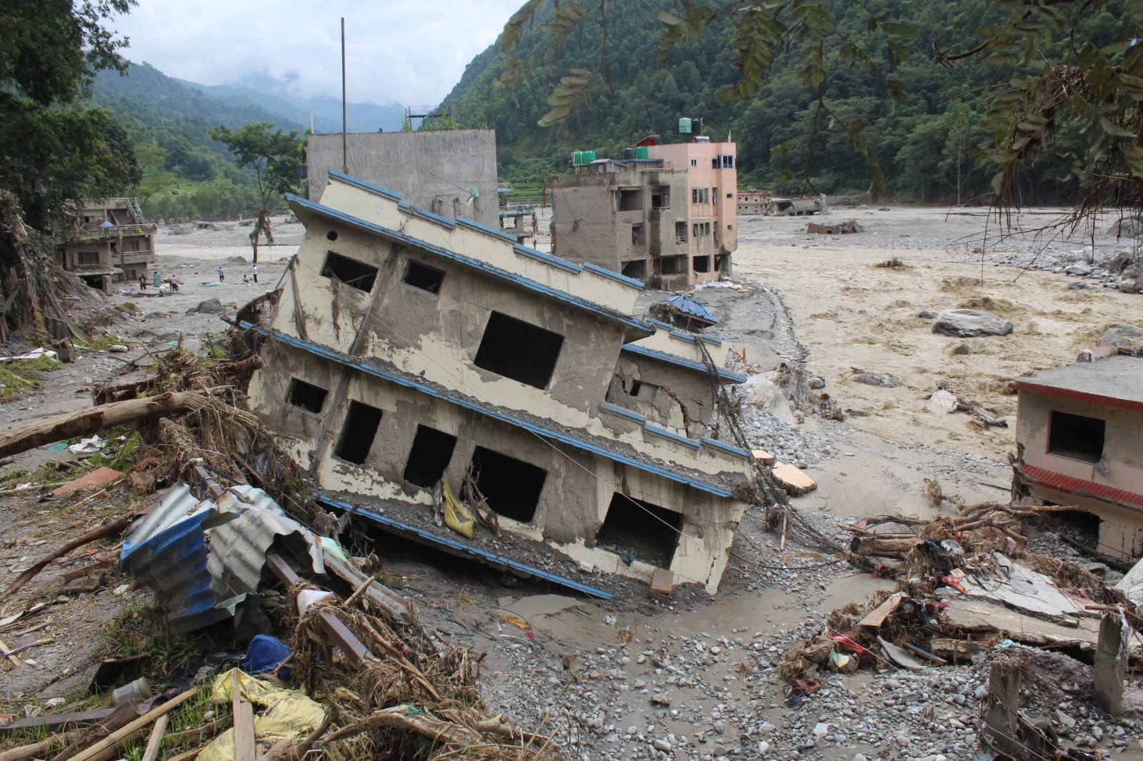 A concrete building tipped onto its side at the edge of the river, its floors collapsed into each other.