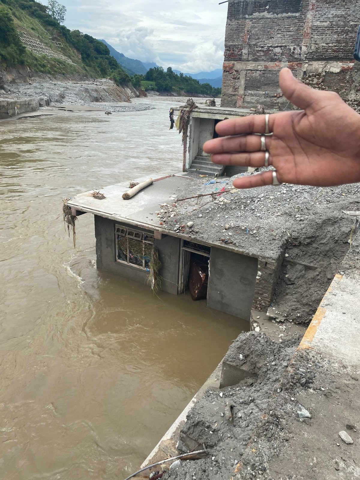 A house submerged up to its roof in a fast moving brown river, with only the top floor and windows above the water.