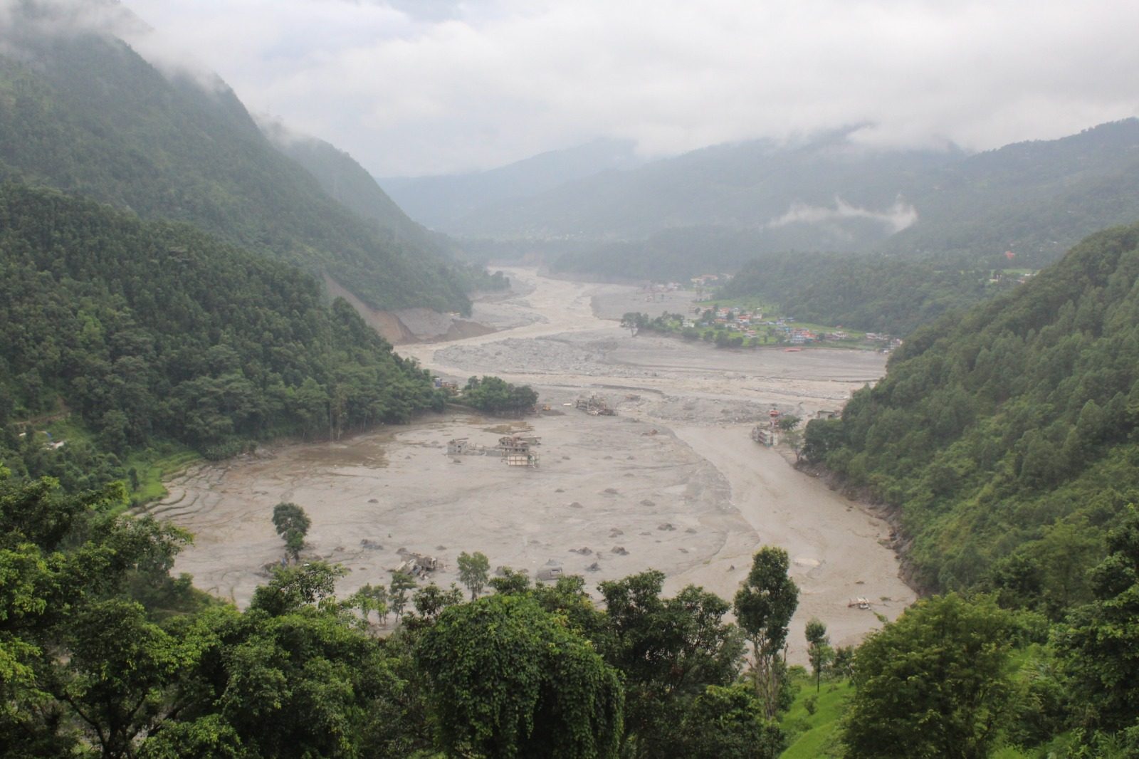 A green Himalayan valley with a wide grey scar of debris running through it where the river used to be.