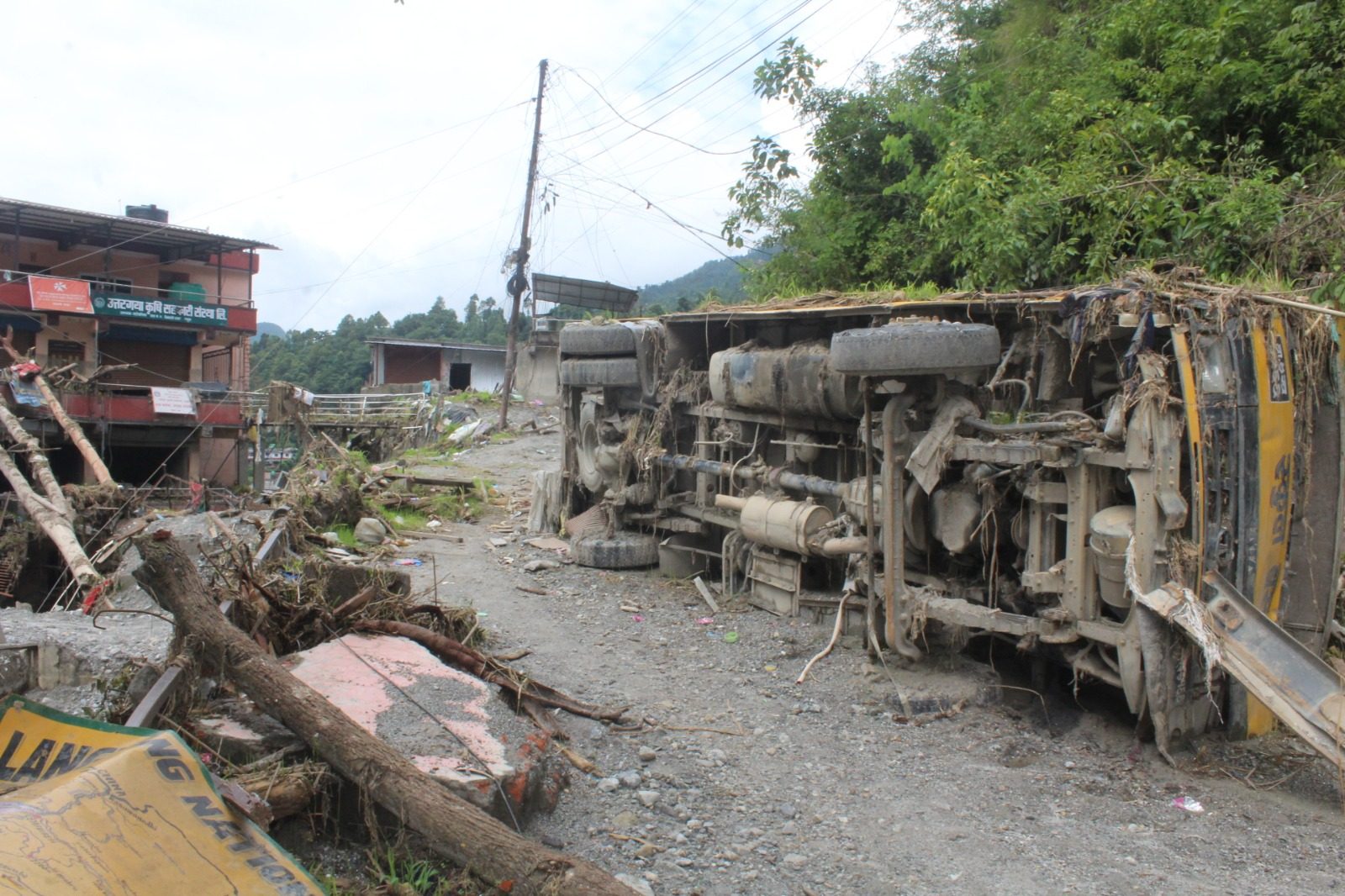 An overturned truck lying on its side on a road covered in mud, with a broken national park sign on the ground nearby.
